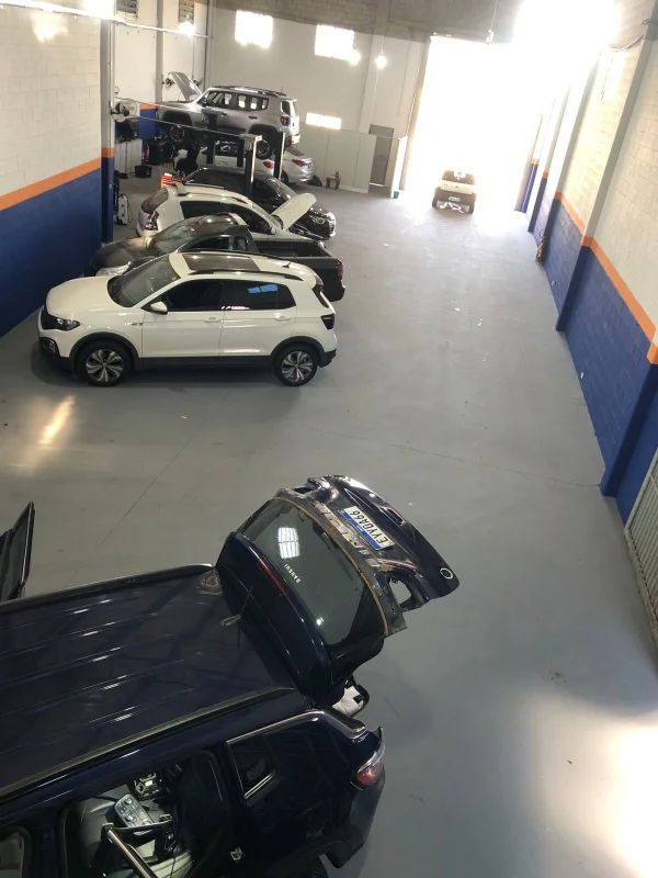 Visão ampla do galpão da oficina mecânica com diversos veículos estacionados e em elevadores