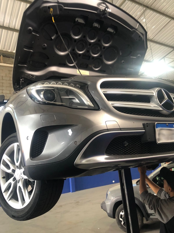 Mecânico realizando manutenção na suspensão de um veículo Mercedes-Benz prateado no elevador