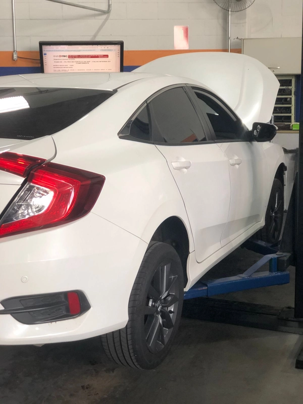 Veículo Honda Civic branco posicionado no elevador automotivo com o capô aberto