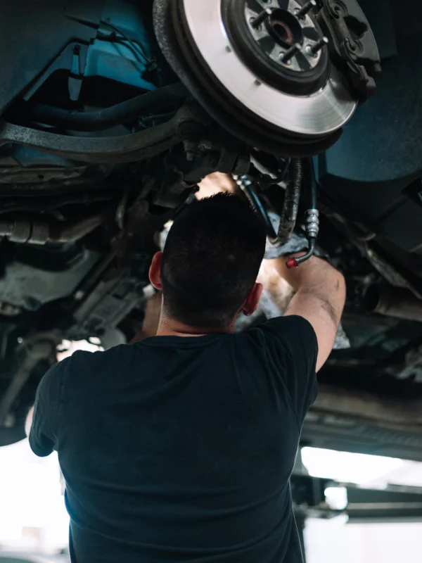 Mecânico posicionado sob o elevador inspecionando detalhadamente os componentes da suspensão
