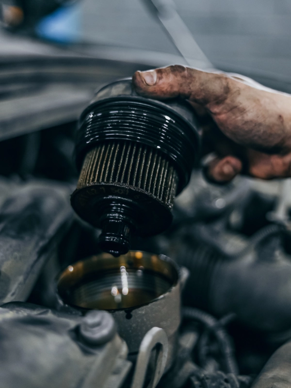 Mão de mecânico exibindo um filtro de óleo antigo, completamente escuro e saturado